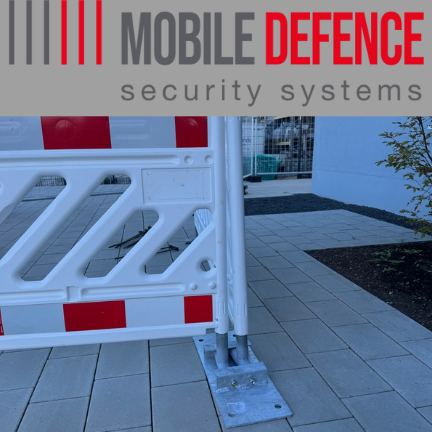 Ein Sicherheitszaun mit rotem und weißem Muster und dem Text "Mobile Defence". Besonders ist der flache Standfuß für mobile Sicherheitszäune